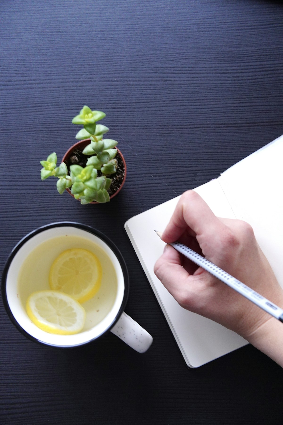 A hand writing in a notebook beside a cup of tea
